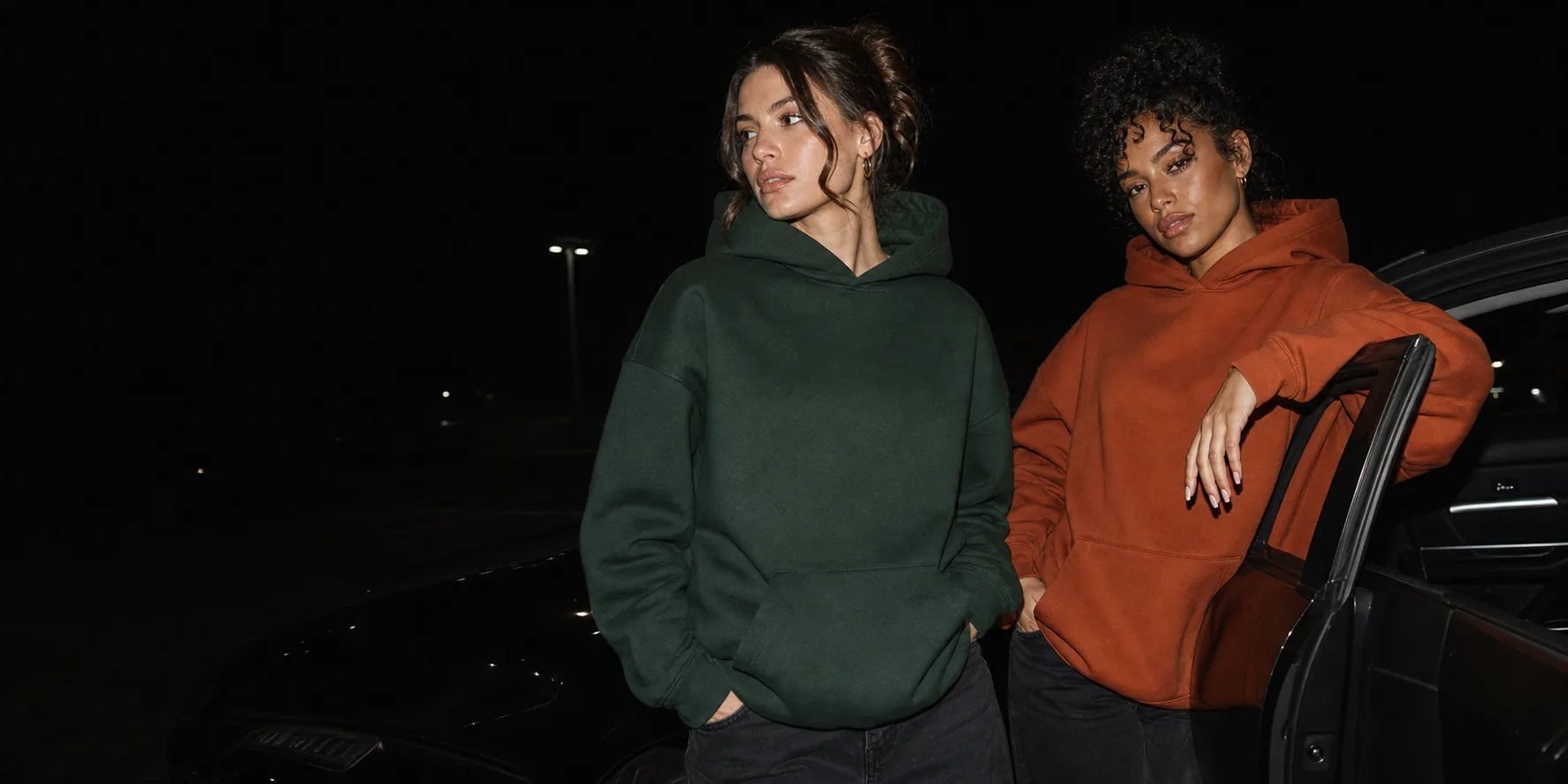 Zwei Models in grünen und terrakottafarbenen Hoodies bei Nacht